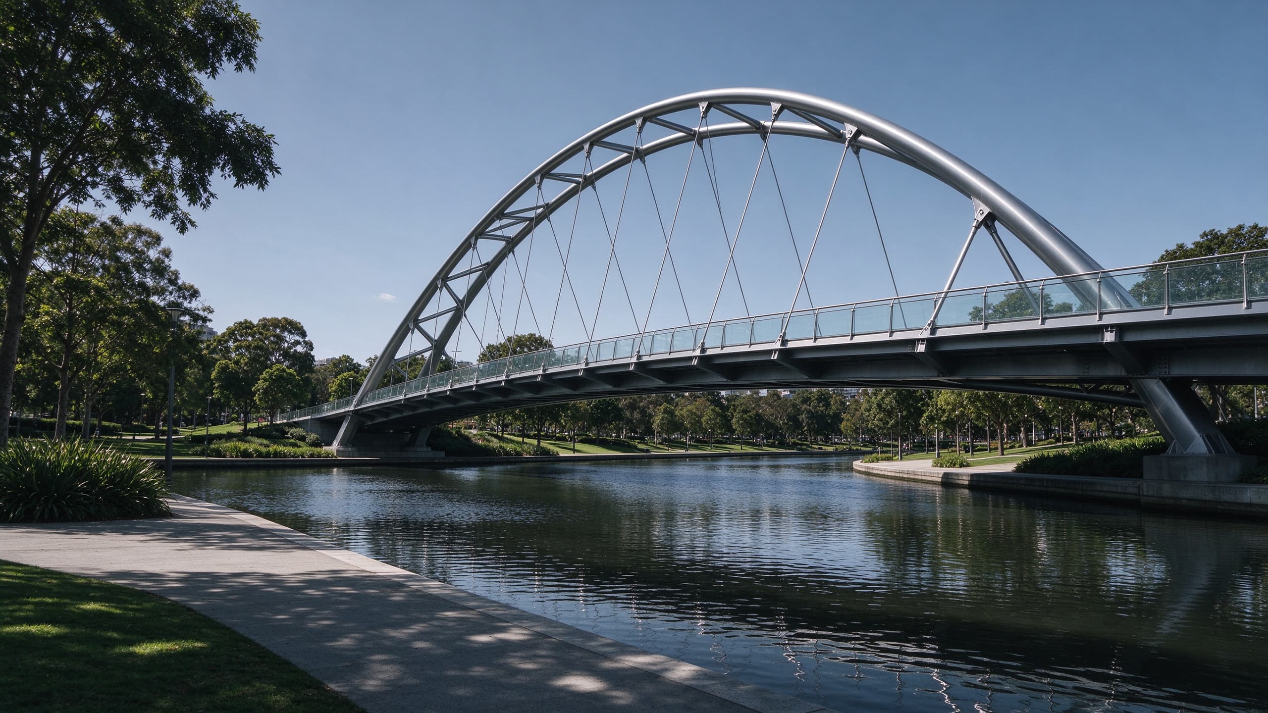 Modern pedestrian steel bridge with arched truss crossing a park waterway